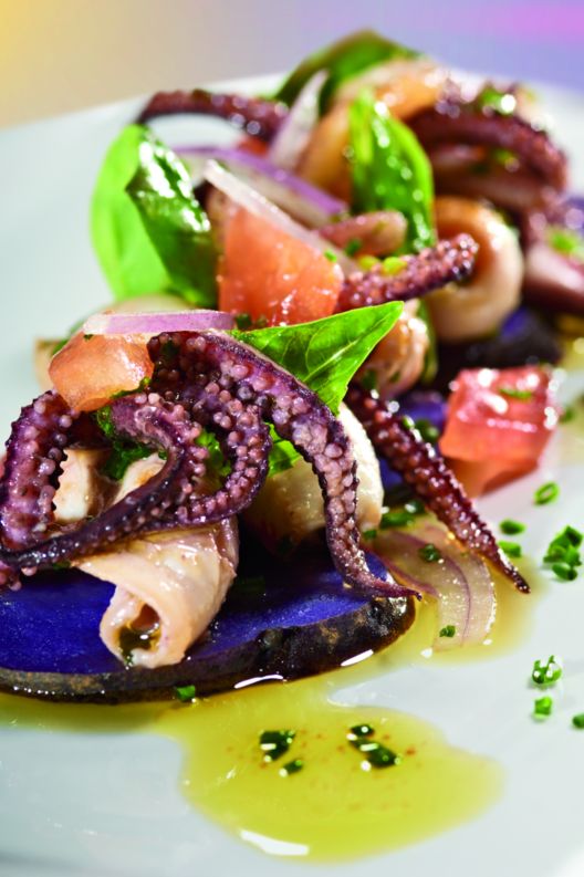 Octopus, greens, tomatoes and fish drizzled in olive oil atop slices of purple potato
