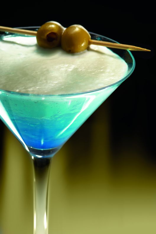 Blue drink with olives on top with a skewer. 