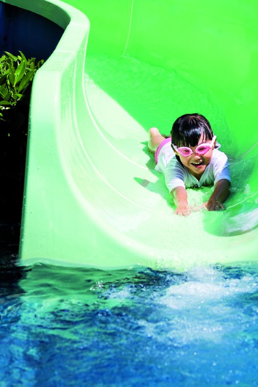 A young girl in swimming goggles sliding head first, on her belly, into a swimming pool.