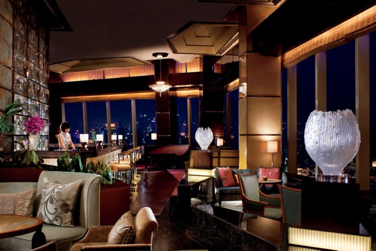 Lounge with walls of floor-to-ceiling windows, versatile and intimate seating and a woman standing behind the bar