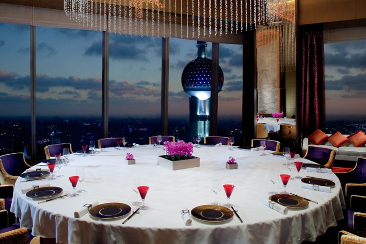Expansive round table with panoramic evening views and an artistic light fixture featuring crystal strings and an orange fish