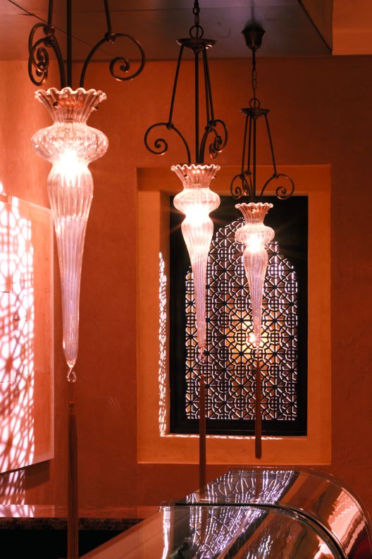 The pattern of a traditional carved screen is reflected on a wall by three dangling light fixtures