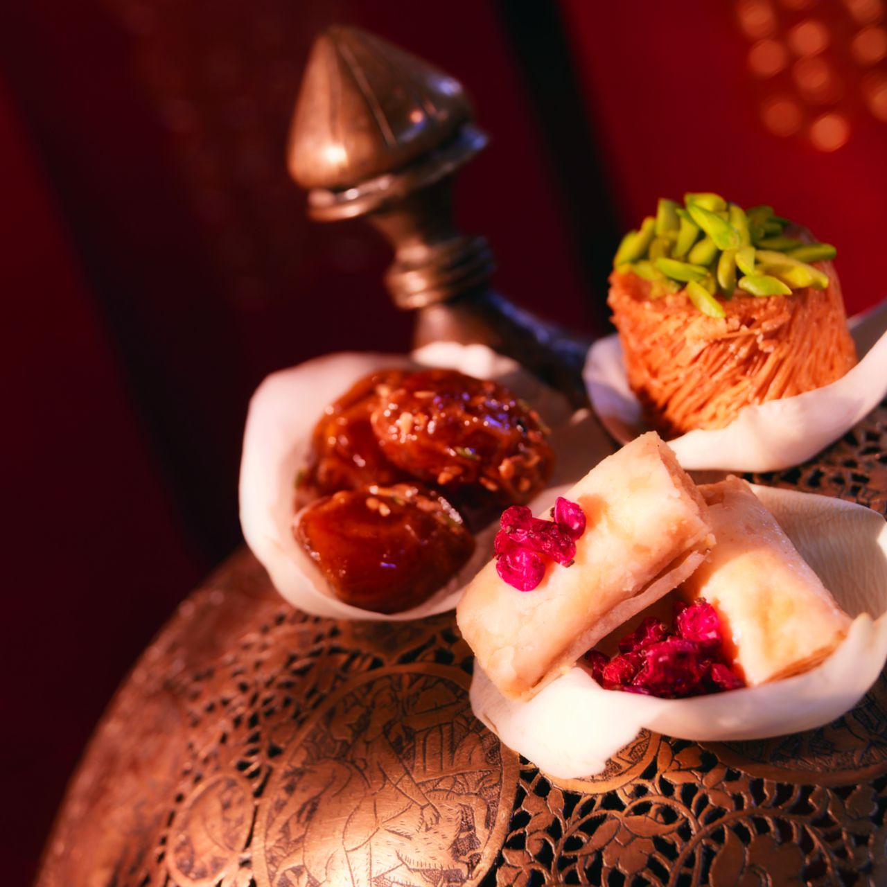 Three bowls of traditional Middle Eastern desserts on a carved table
