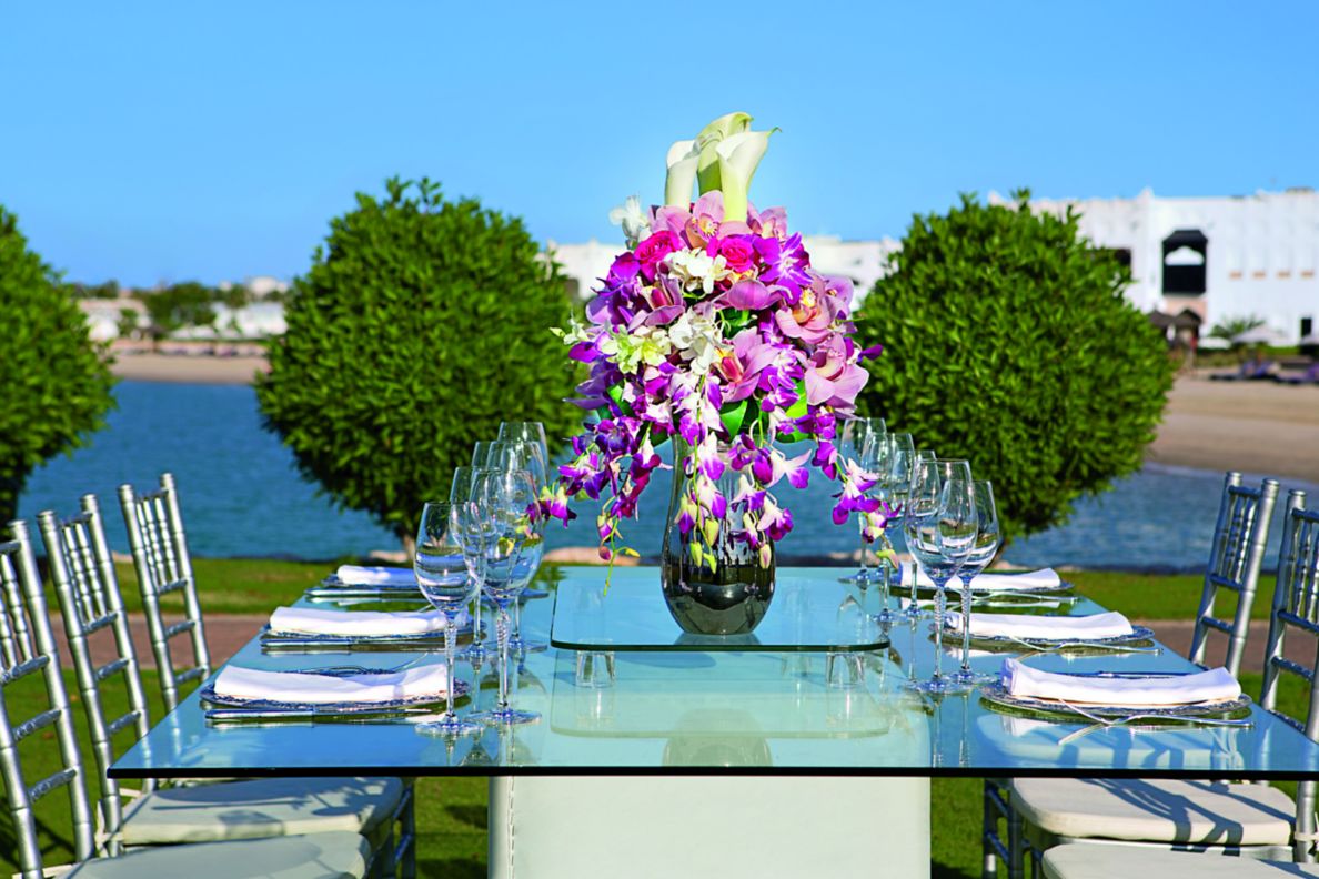 A table set for eight outside in a garden with purple flowers as the centerpiece.
