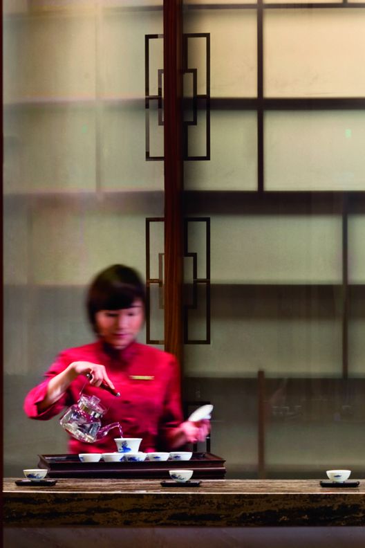 Woman pouring tea at a wood counter with tea cups spaced evenly across it