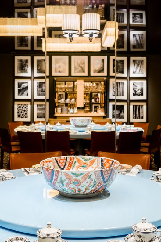 Rust-colored chairs surround a circular, powder-blue table with a lazy Susan and which is set with colorful Chinese plates