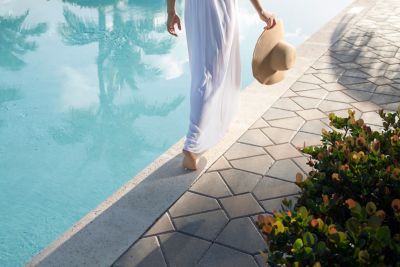 Legs of woman holding hat walking alongside the pool