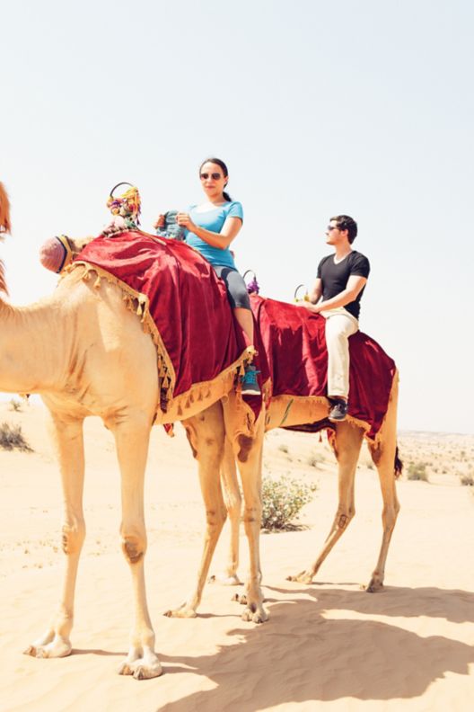 Two people riding camels in desert. 