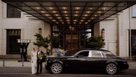 Wedded Couple by Car in front of hotel entrance