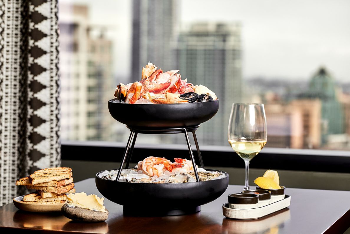 Two-tier tray with seafood on ice in front of window with a city view. 