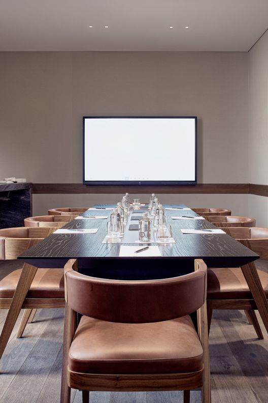 Meeting room with long wooden table, mounted television screen, coffee set-up. 
