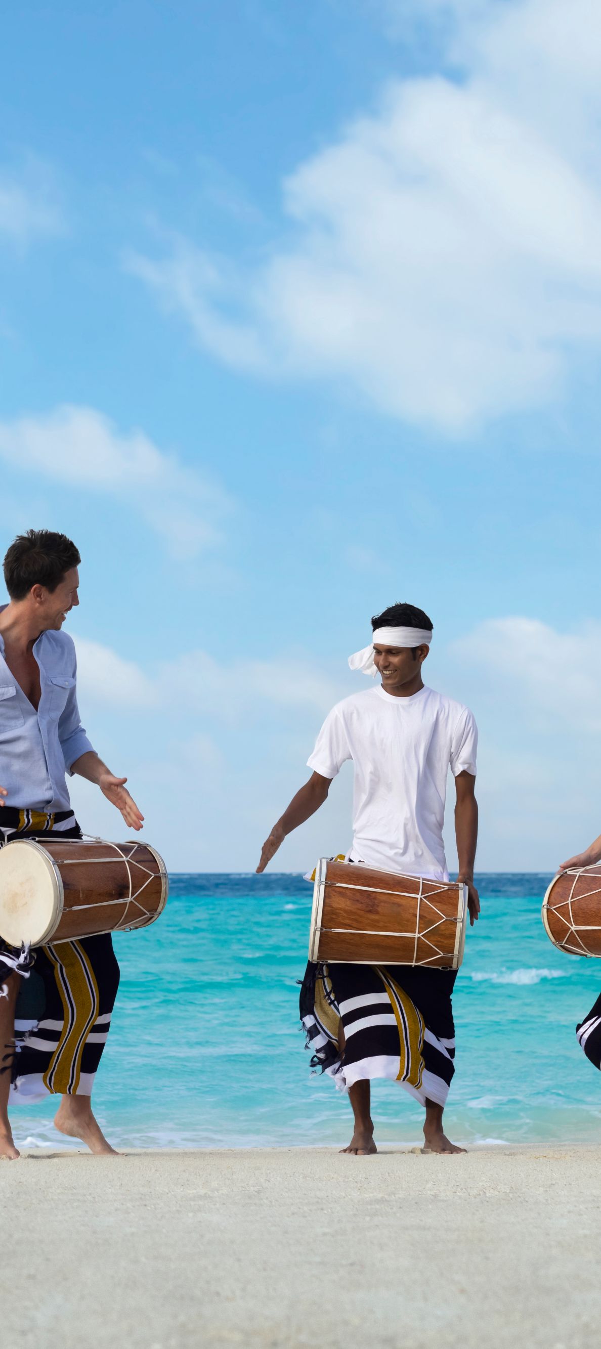 Three people on the beach with Bodaberu drums with the ocean in the background.