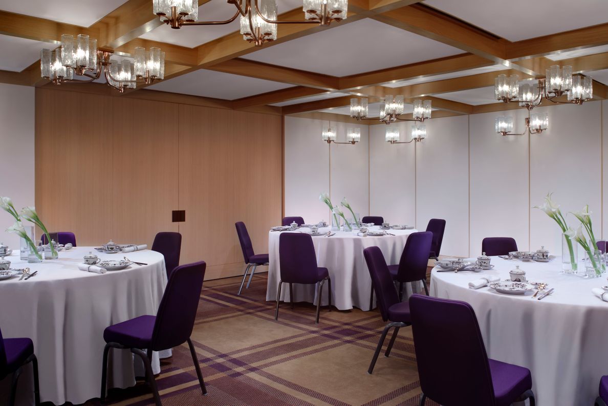 Meeting room with round tables, chairs, silverware and lights above.