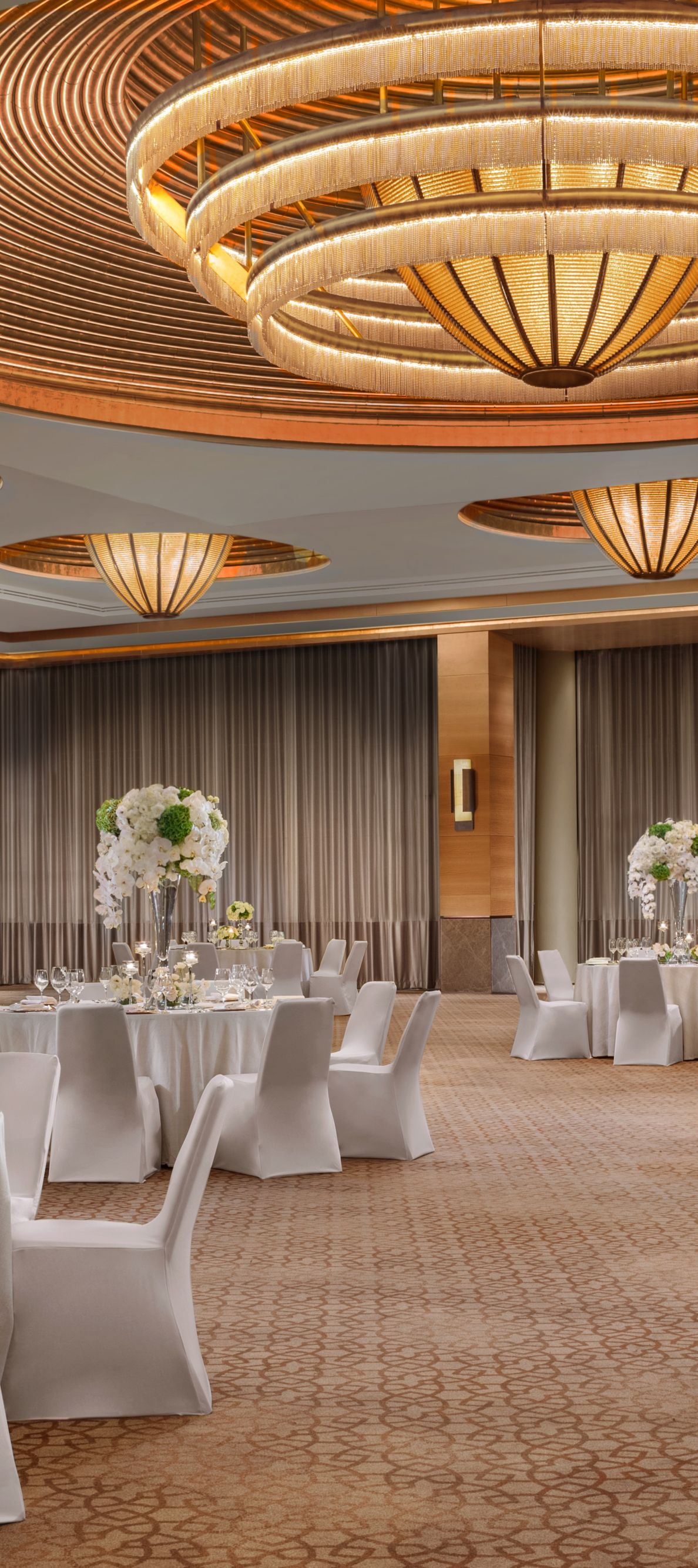 Grand Ballroom with floral decorations and silverware on white cloth round tables and chairs.