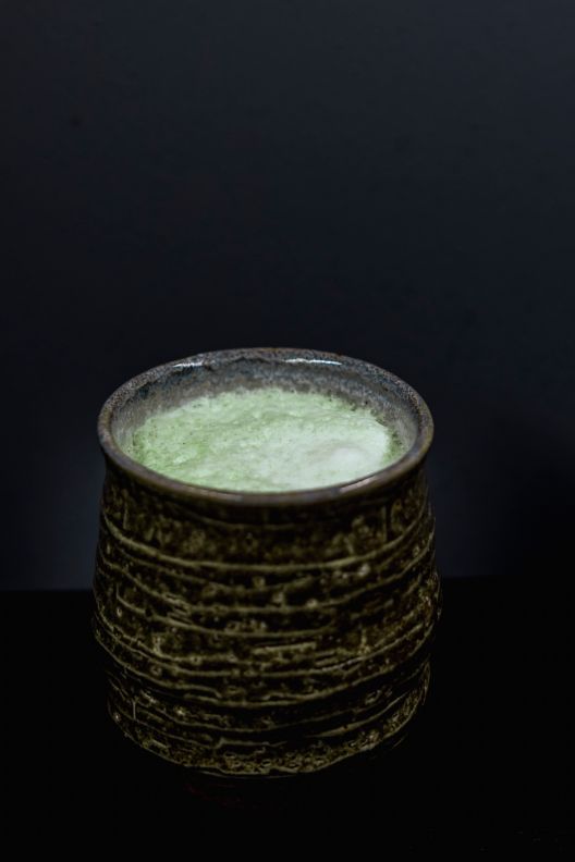 Cup with mint green ingredients within and a dark background. 