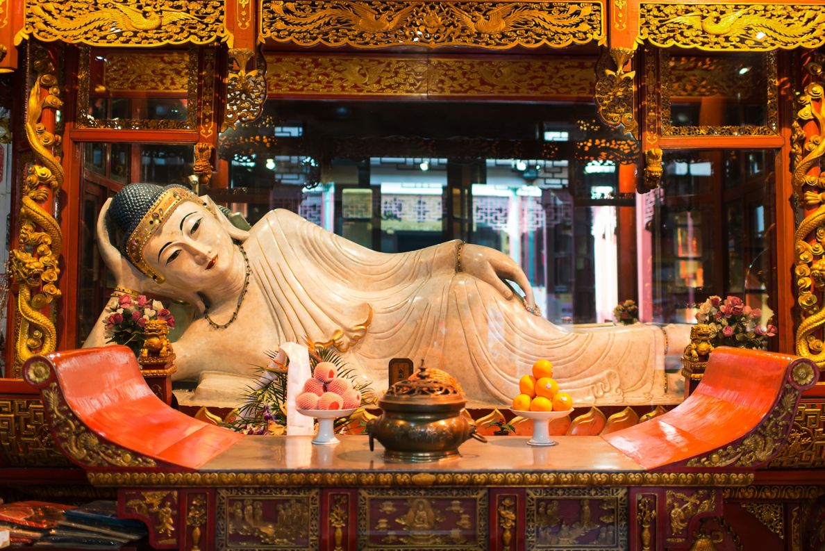 Buddha statue laying on its side in front of bench with bowls of fruit. 