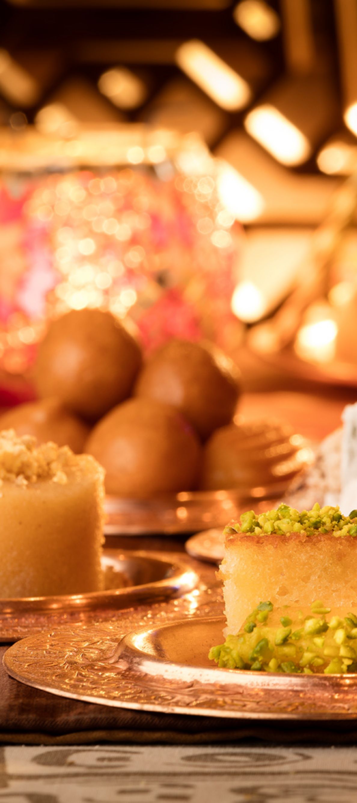 Gold plates bearing sweet treats are presented on an intricately designed table next to colorful, spherical candle holders