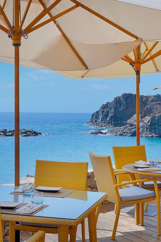 Umbrellas covering dining tables and chairs with a view of the ocean.