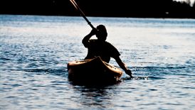 Silhouette of a man kayaking alone on the blue water of the ocean