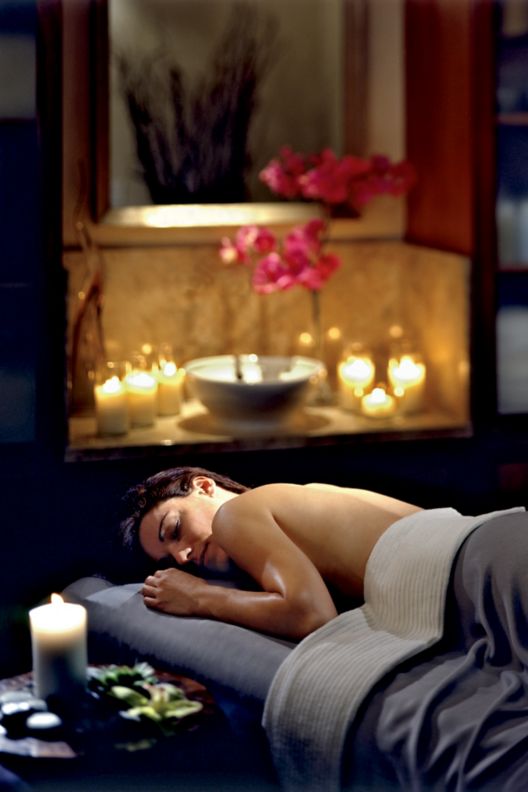 Woman laying down on a massage bed with lit candles in the background.