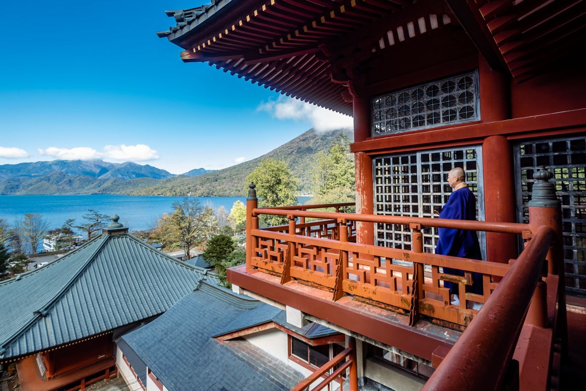A monk walking along a balcony at Chuzenji temple, with lake in background.