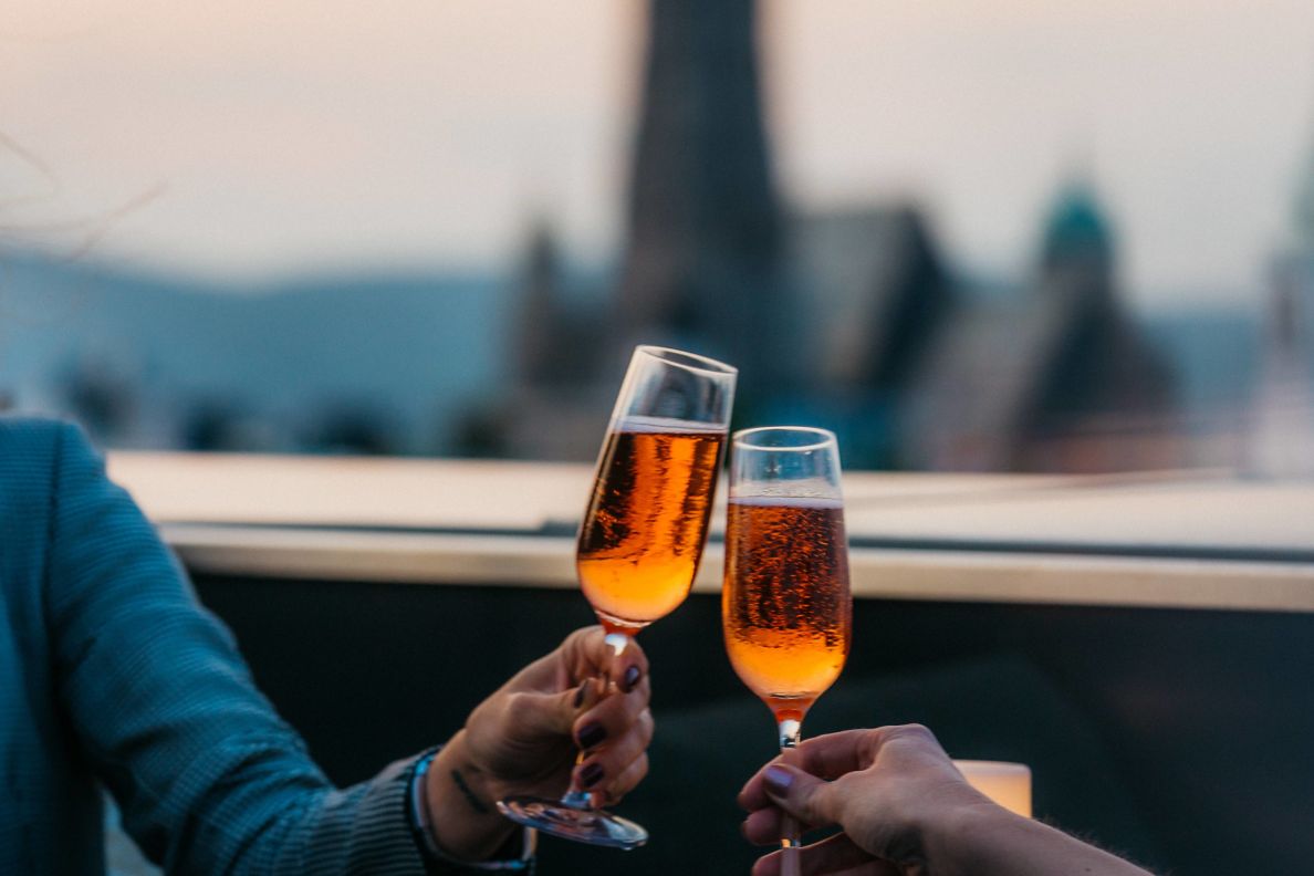 A couple on the rooftop clinking glasses with the view of Vienna in the background.