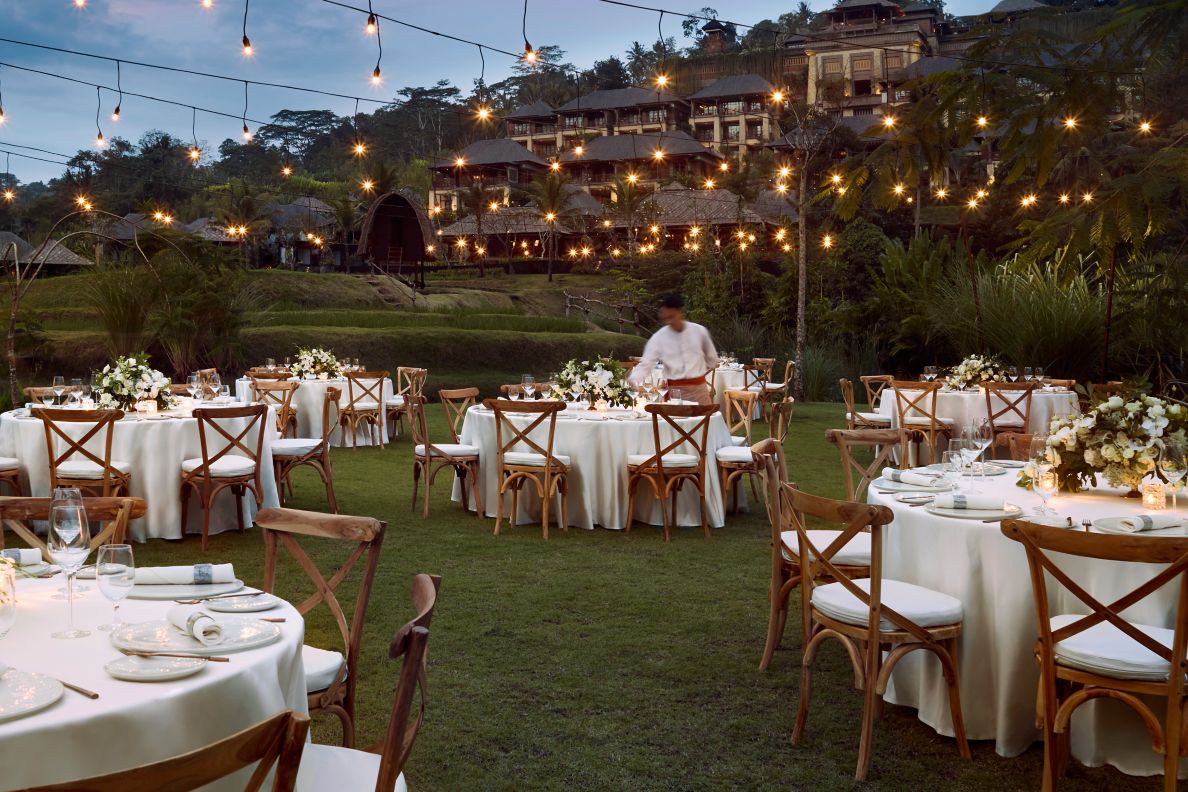 Outdoor reception with white round tables and string lights.