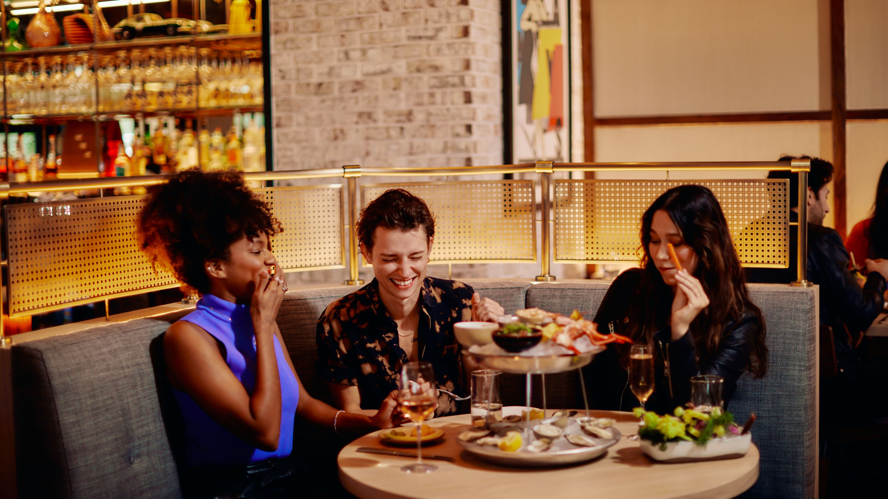 Three people sitting in a booth at a restaurant  with a table filled with different plates.