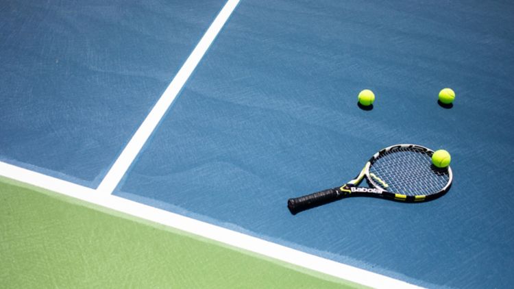 Tennis racket and tennis balls laying on tennis court.