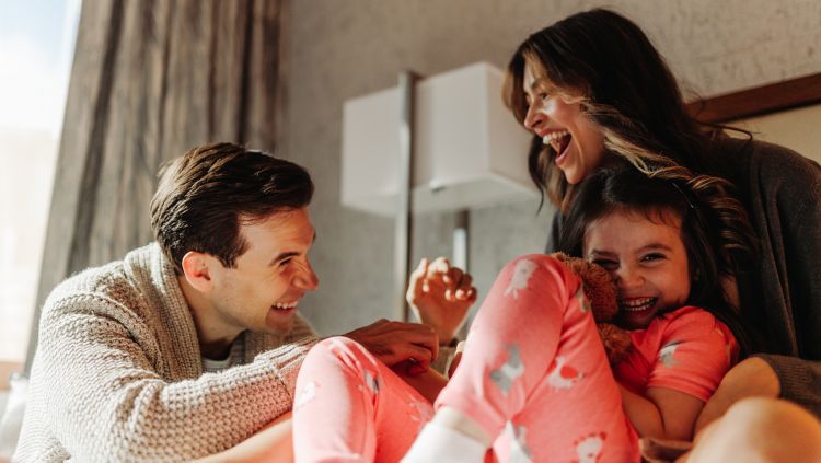 A family sitting together on a bed and laughing.