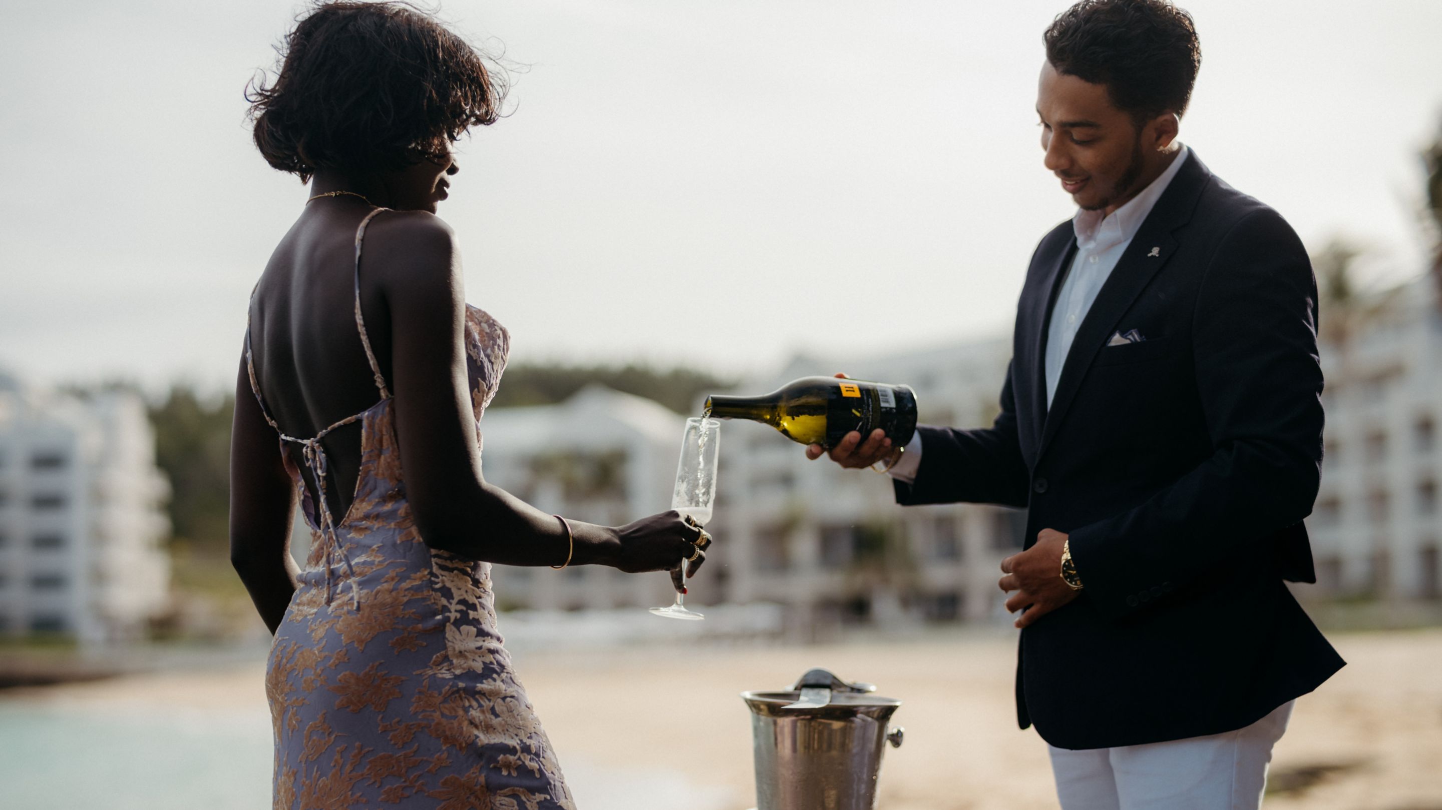 A couple standing together outside pouring wine into glasses.