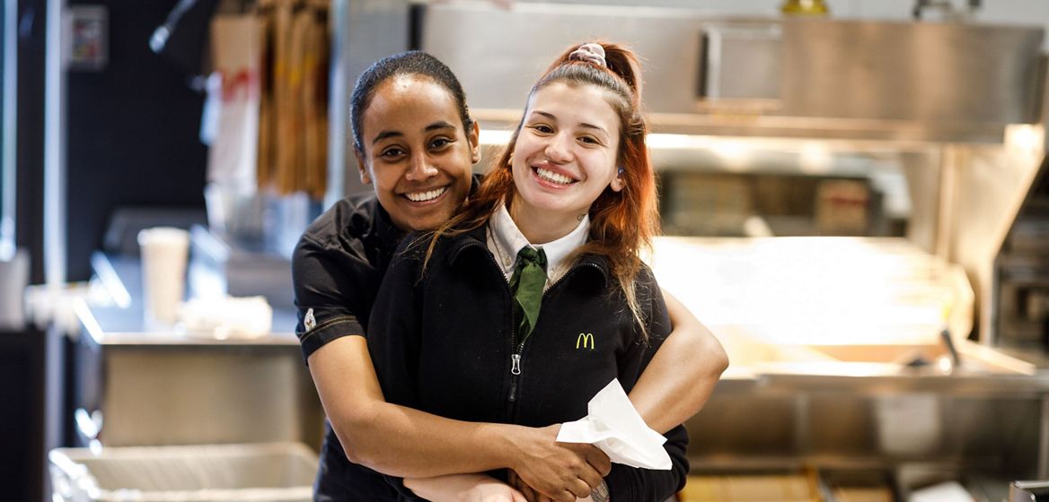Two smiling McD employees are holding each other