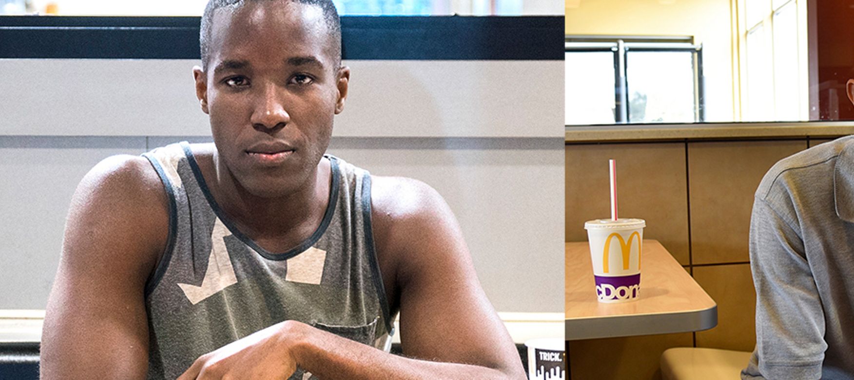 Man in tank top stares into camera while sitting at a table and enjoying a mcdonalds burger and fries and a man in grey polo and folded hands sits on the end of a McDonald's booth