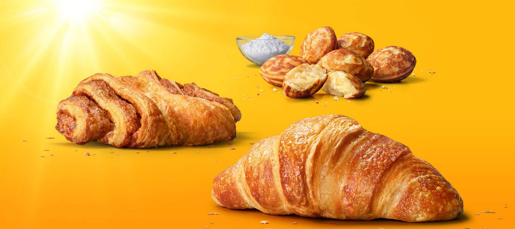Das Bild zeigt ein Franzbrötchen, ein Buttercroissant und Mini Pancakes mit Puderzucker.