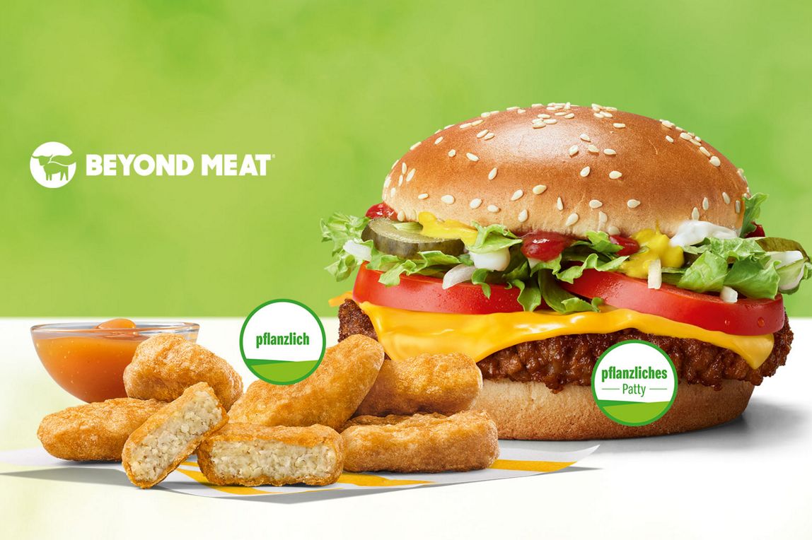 Ein McPlant® auf dem “pflanziliches Patty“ steht. Daneben McPlant® Nuggets, auf denen „pflanzlich“ steht vor einem Schälchen Süß-sauer Sauce. Darüber steht Beyond Meat.
