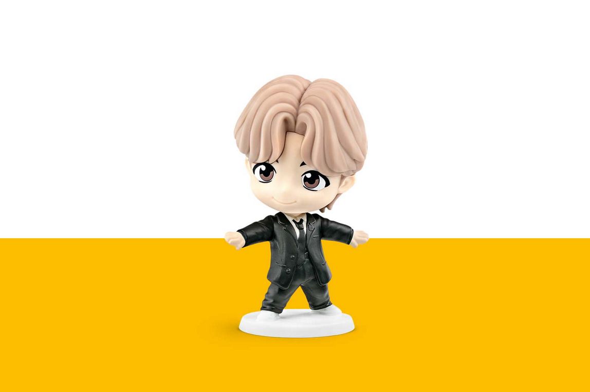 Jung Kook hat blonde Haare und trägt einen schwarzen Anzug mit Anzug-Weste darunter. 