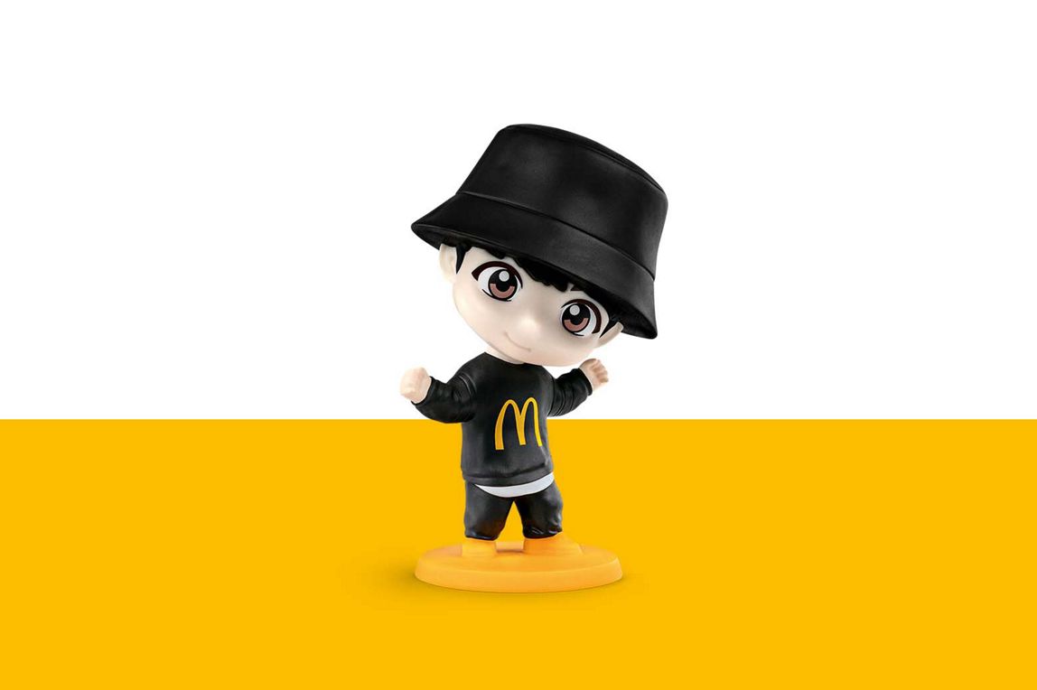 Jung Kook trägt einen schwarzen Anglerhut und hat ein schwarzes Outfit an mit einem goldenen M auf der Brust.