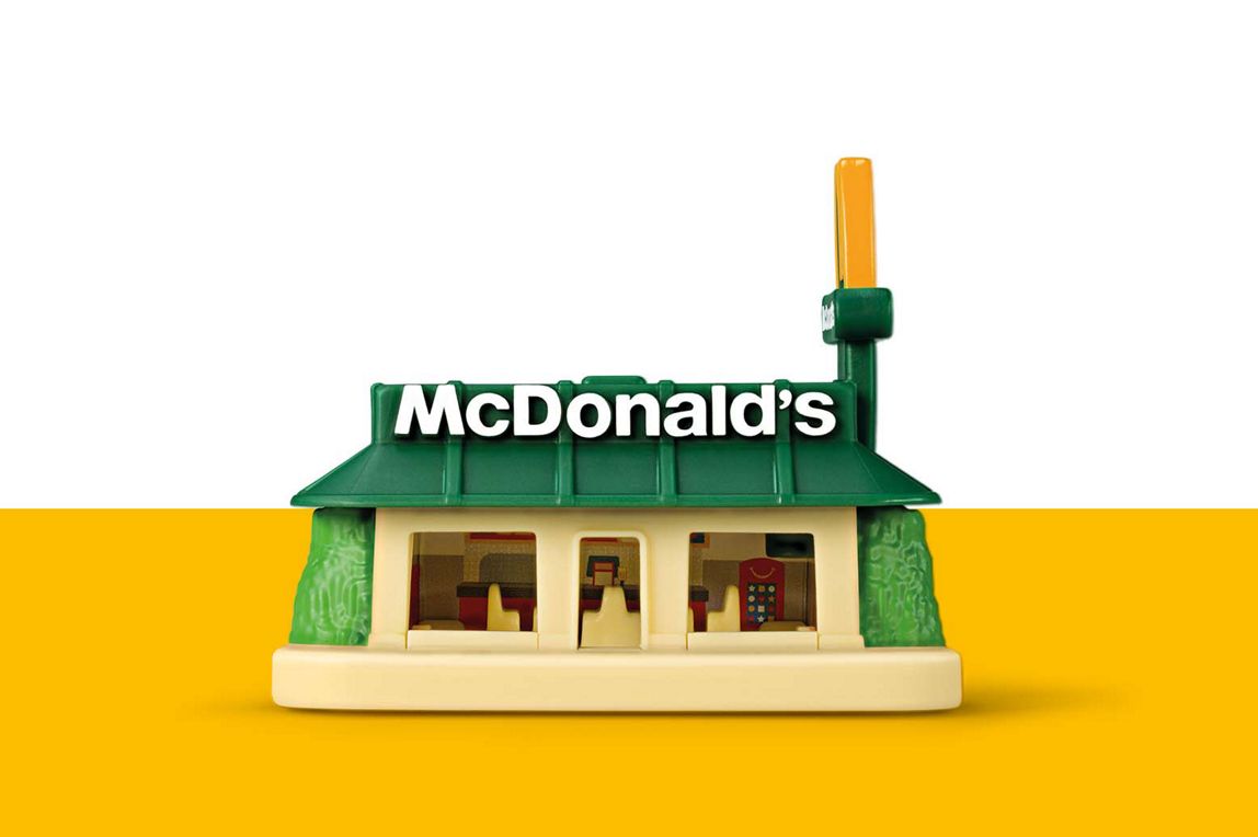 Ein Spielzeug-Modell eines McDonald's Restaurants mit grünem Dach, beiger Fassade und dem McDonald's Schriftzug.