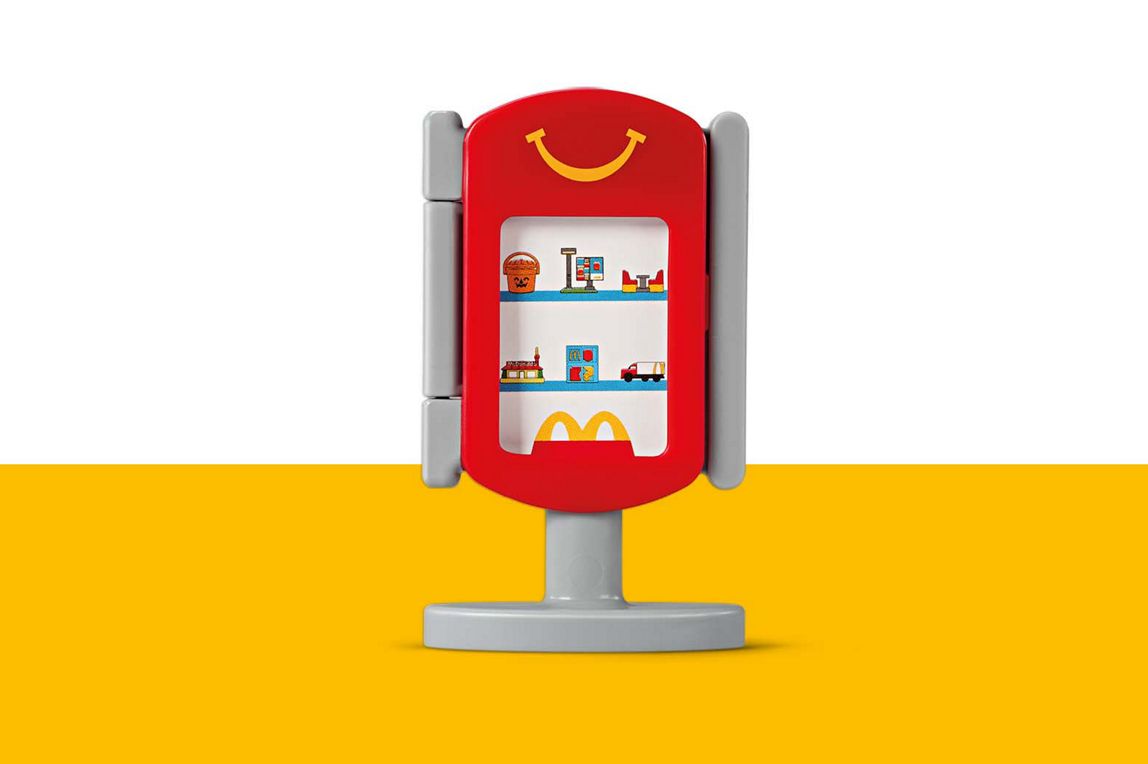 Ein roter Spielzeug-Displayständer mit einem lächelnden Gesicht, kleinen Spielzeugen auf Regalen und dem goldenen McDonald's Logo.