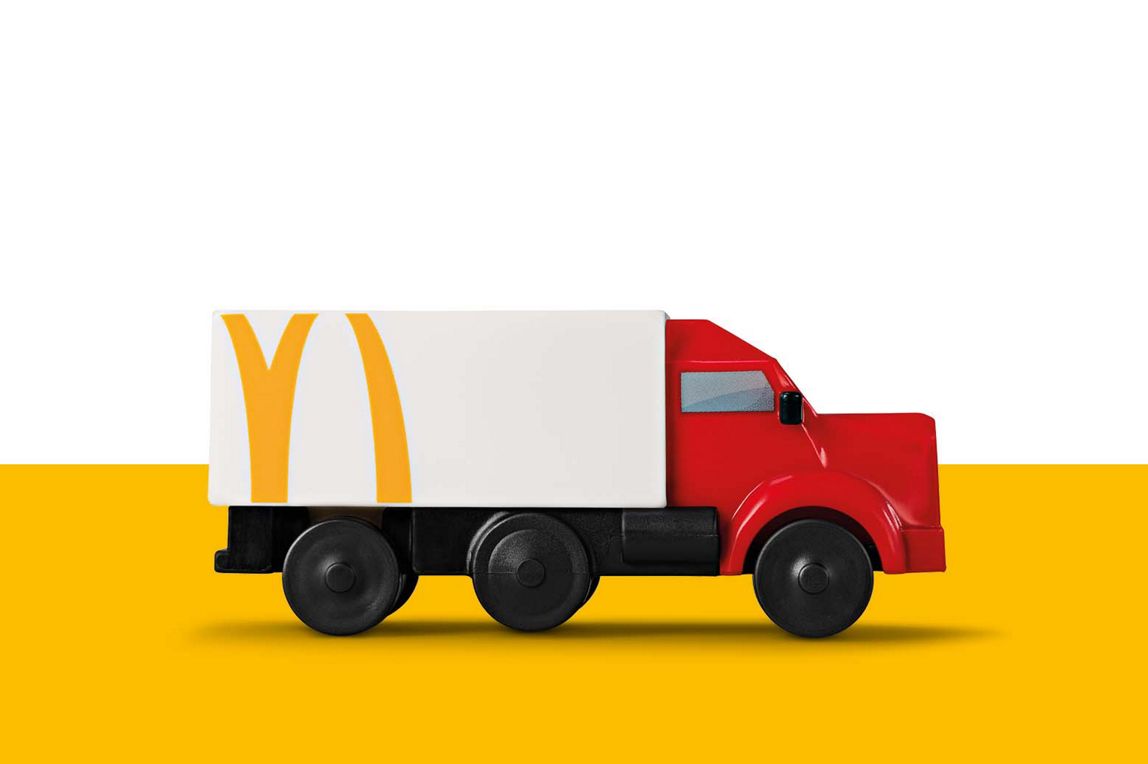 Ein weißer Spielzeug-Truck mit angeschnittenem gelben „M“ auf der Seite und einer roten Fahrerkabine.