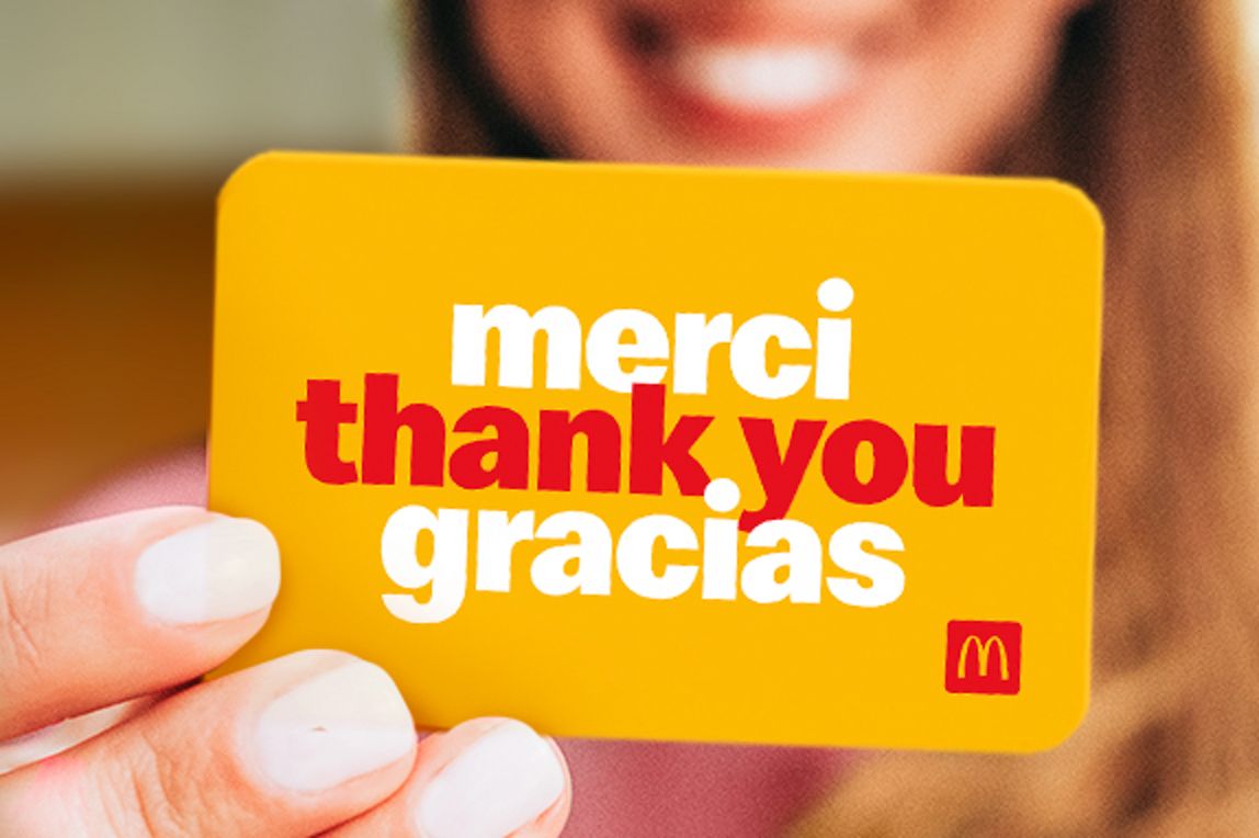 a woman smiling and holding an Arch Card that reads “merci, thank you, gracias”