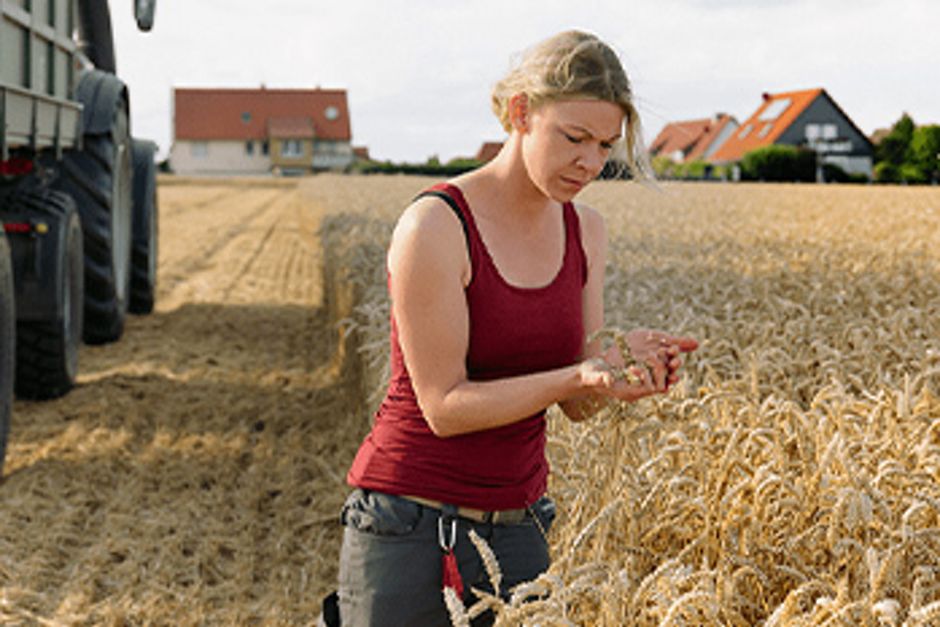 Eine Bäuerin auf em Feld neben einem Traktor