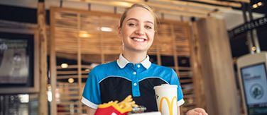 Lächelnde McDonald's Mitarbeiterin mit McMenü®-Tablett in den Händen