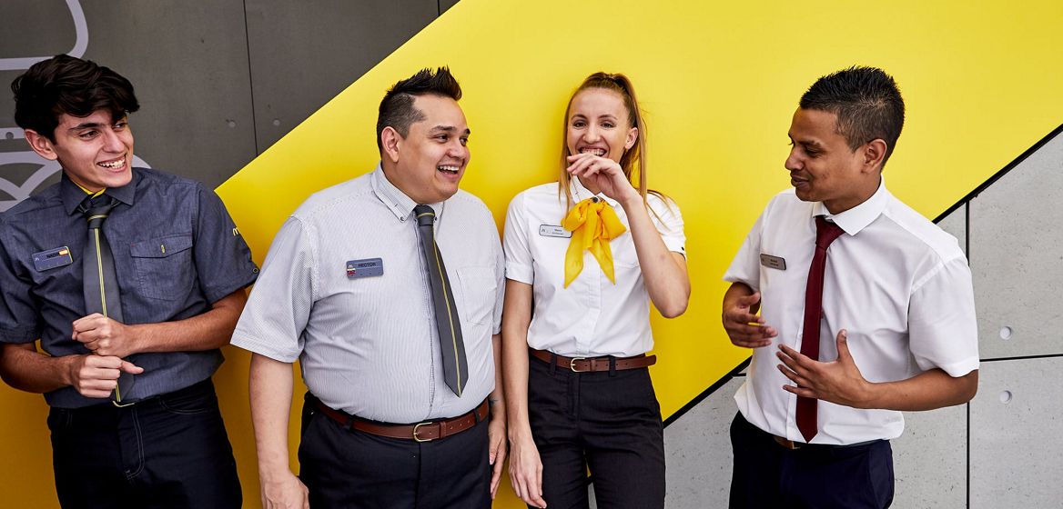 Four McDonald's employees standing together outside of a restaurant smiling and laughing