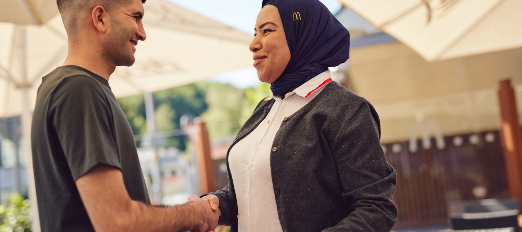 McDonald’s-Mitarbeiterin mit Kopftuch begrüßt einen Mann per Handschlag.