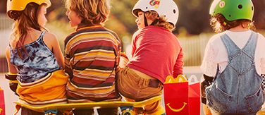 Vier Kinder in Rückansicht machen mit einem Happy Meal® Pause vom Skateboardfahren