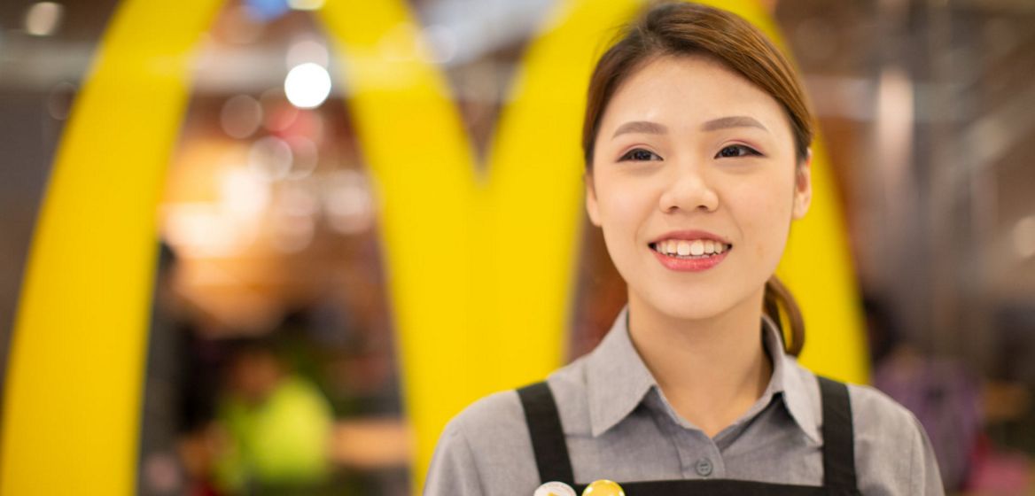 A McDonald's employee standing in front of the McDonald's logo