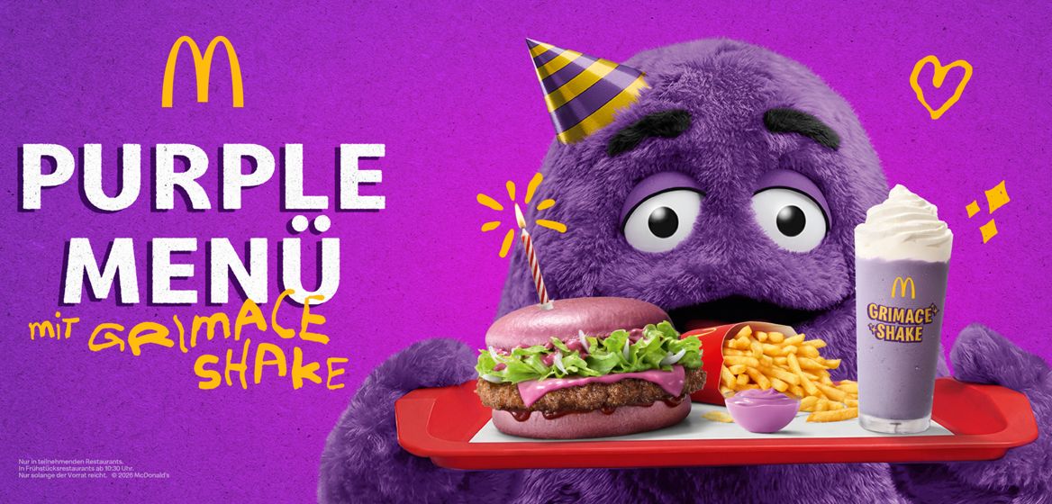 Die Figur Grimace hält ein Tablett in der Hand, auf dem ein Purple BBQ, Purple Dip, Grimace Shake und Pommes liegen; links daneben steht "Purple Menü mit Grimace Shake".