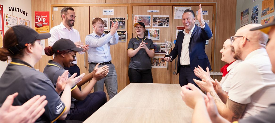 Multi-site franchisee Carel Venter and team applauding a manager holding a trophy in the crew room.
