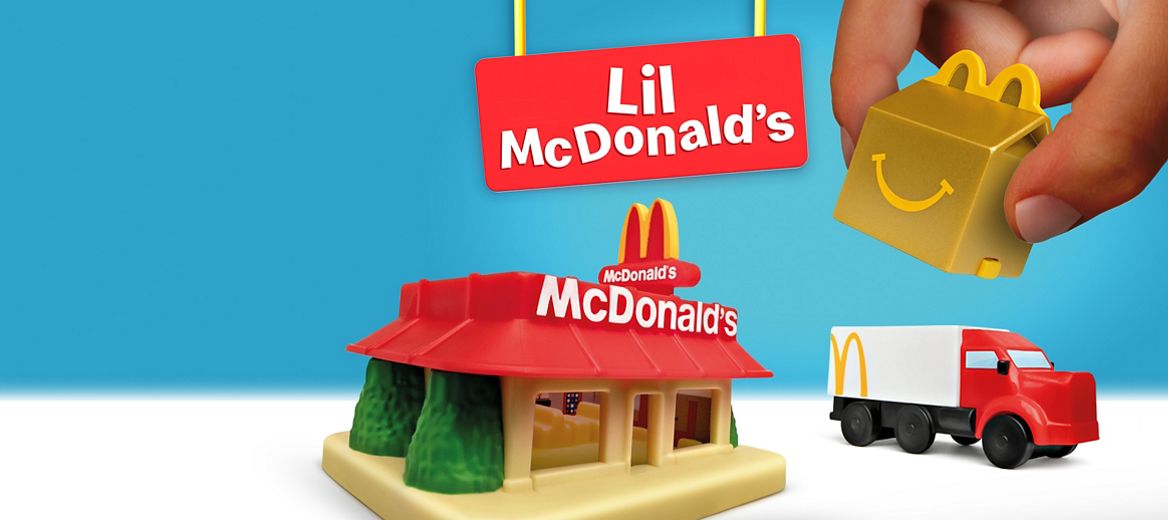 Une main tenant une boîte à Joyeux festin dorée miniature se trouve à côté d’un restaurant McDonald’s de style rétro miniature et d’un camion de livraison miniature. Le logo Lil McDonald’s est tout en haut.